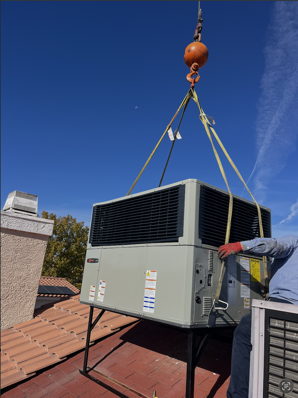ACTS Inc technician guiding a rooftop HVAC unit into place by crane